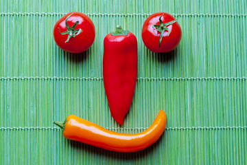 Smiling face of fresh vegetables on green bamboo placemat.