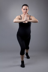 Pregnant woman doing gymnastic exercises on grey background.