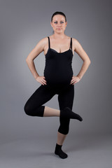Pregnant woman doing gymnastic exercises on grey background.