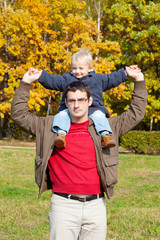 small son sits on shoulders at  father. Walk in autumn park