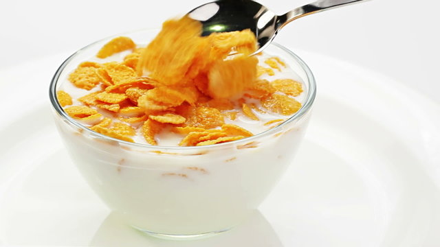 Cooking corn flakes with milk in a glass bowl stirring by spoon