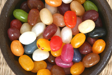 Colourful candies in a brown bowl on white background