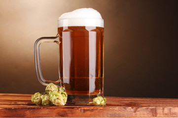 beer mug and green hop on wooden table on brown background
