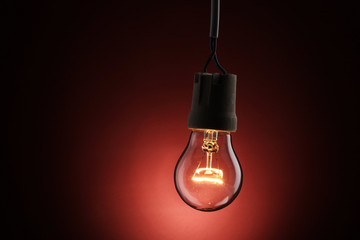 A lit light bulb on red background