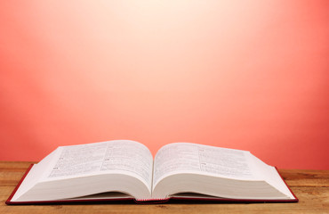 Open book on wooden table on red background