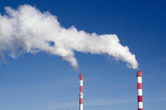 Pair of industrial chimneys with lots of smoke on a blue sky