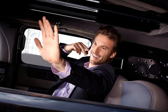 Young celebrity waving from limousine smiling