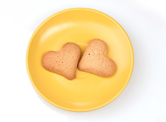 Two heart-shaped cookies on yellow saucer isolated on white