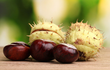 green and brown chestnuts on wooden table on green background