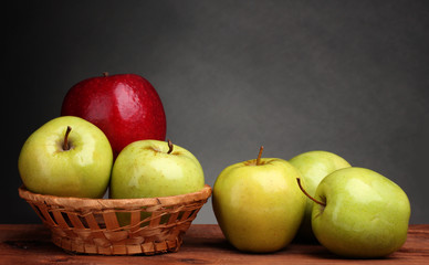 juicy sweet apples in basket on wooden table on gray background