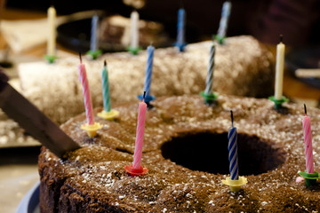 Ein Messer schneidet in einen Geburtstagskuchen mit Kerzen in Form eines Gugelhupf