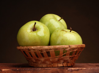 juicy green apples in basket on wooden table on brown background