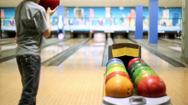 Little boy takes bowling ball and throws it to beat skittles