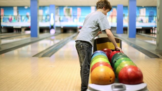 boy takes one of bowling balls and throws it to beat tenpins