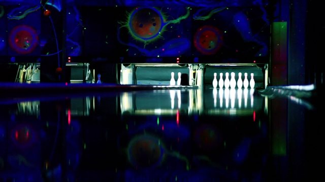 Skittles at bowling lane lit in dark club, people throw balls