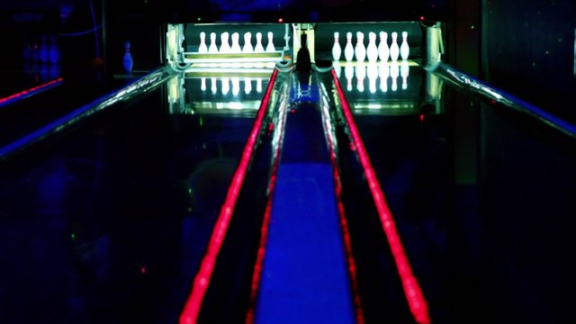 Two bowling lanes lit in dark club, bolls roll and beat tenpins