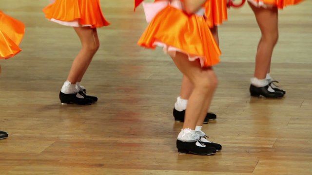 Five girls in shoes with taps and orange skirts tap dance