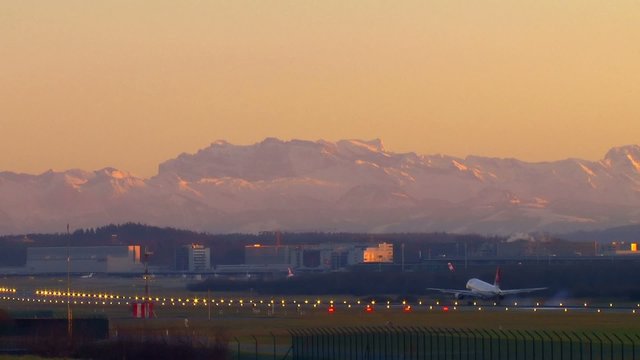Flugzeug landet im Abendlicht vor Alpenkulisse