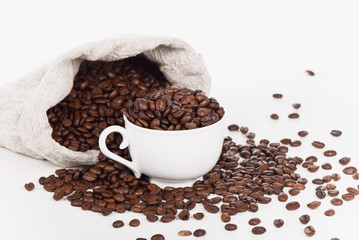 cup lies in a sack with coffee grains is isolated on white
