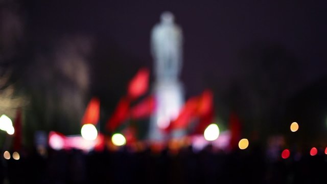 Crowd with red flags in front of monument at night