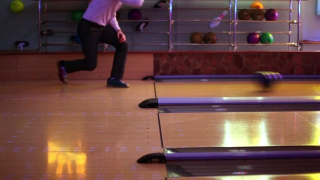 Two men throw bowling ball on parallel lanes in club
