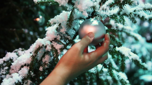 ball hangs on snow covered fir, gentle female hand touches it