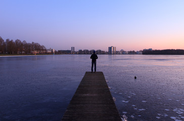 Man looking at the ice of a frozen lake near a city