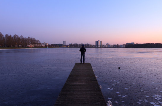 Man looking at the ice of a frozen lake near a city