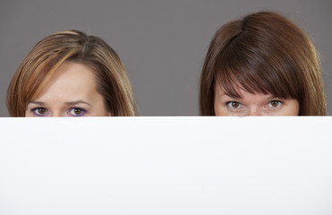 two women peeking over white banner