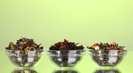 Different kinds of green and black dry tea on green background