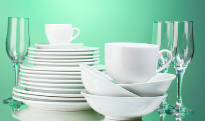 Clean plates, cups and glasses on green background