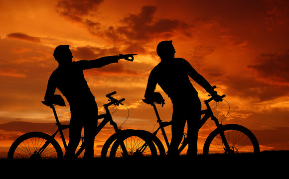 two mountain bikers silhouette in sunset