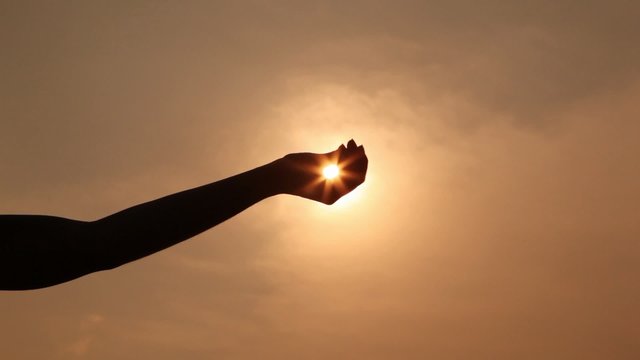 hand silhouette holds sun on palm