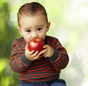 portrait of a handsome kid sucking a red apple at park