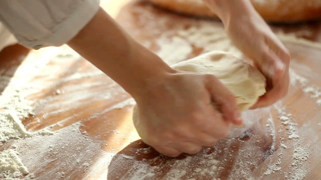 Baker hands kneading dough in flour on table, slow motion