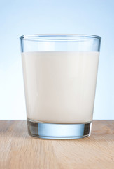 Glass of fresh milk is wooden table on a blue background