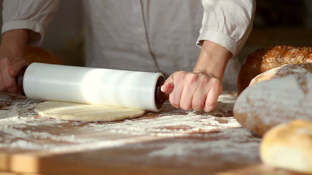 Baker kneading dough with rolling pin on table, slow motion