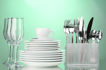 Clean plates, glasses, cup and cutlery on green background