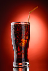 Glass of cola with ice on red background