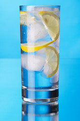 Glass of lemon ice water on blue background