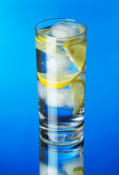Glass of lemon ice water on blue background