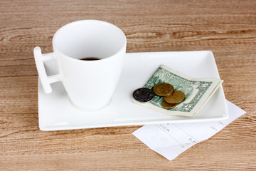 Empty cup of coffee with five dollars tip on wooden background