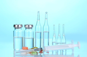 Syringe with medical ampoules and tablets on blue background