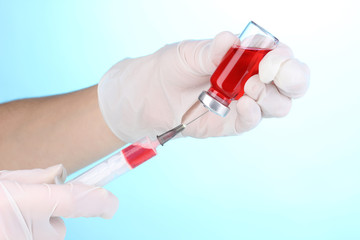 Syringe and medical ampoule in hands on blue background