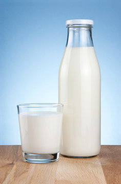 Bottle of fresh milk and glass is wooden table on a blue backgro