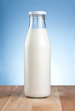 Bottle of fresh milk is wooden table on a blue background