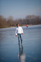Naklejka premium Handsome young man ice skating outdoors on a pond