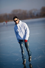 Handsome young man ice skating outdoors on a pond