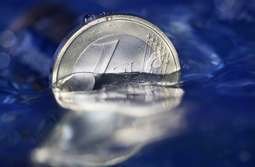 1 Euro Münze versinkt in blauem Wasser als Symbol für Wirtschaftskrise