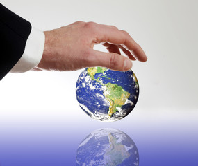 Mann mit Anzug legt beschuetzend seine Hand ueber die Erde